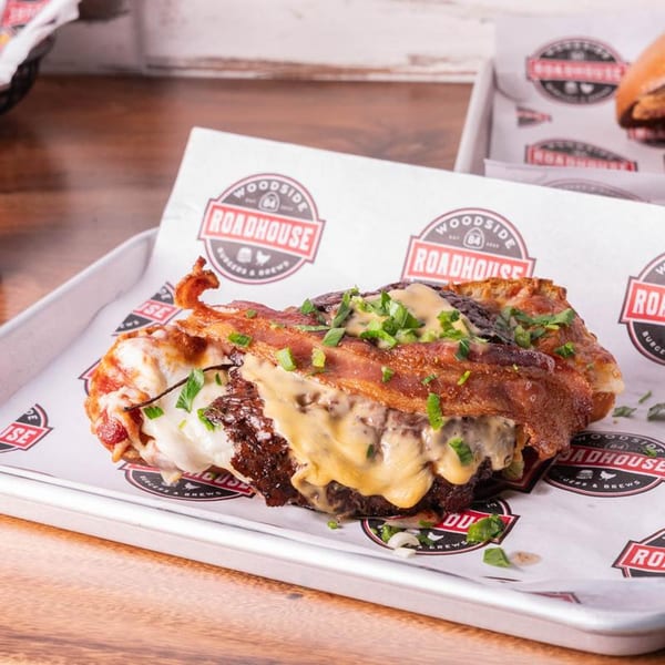 A Woodside Roadhouse burger patty wrapped in bacon and topped with melted cheese and chives.