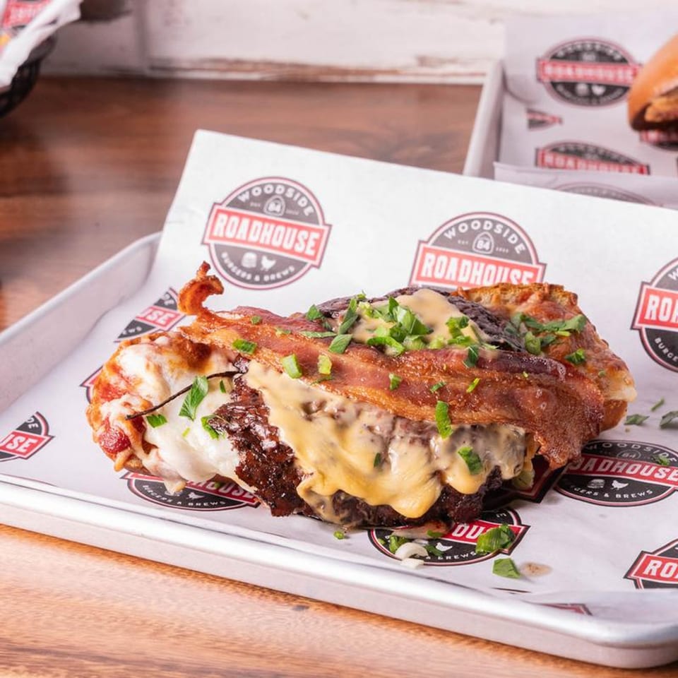 A Woodside Roadhouse burger patty wrapped in bacon and topped with melted cheese and chives.