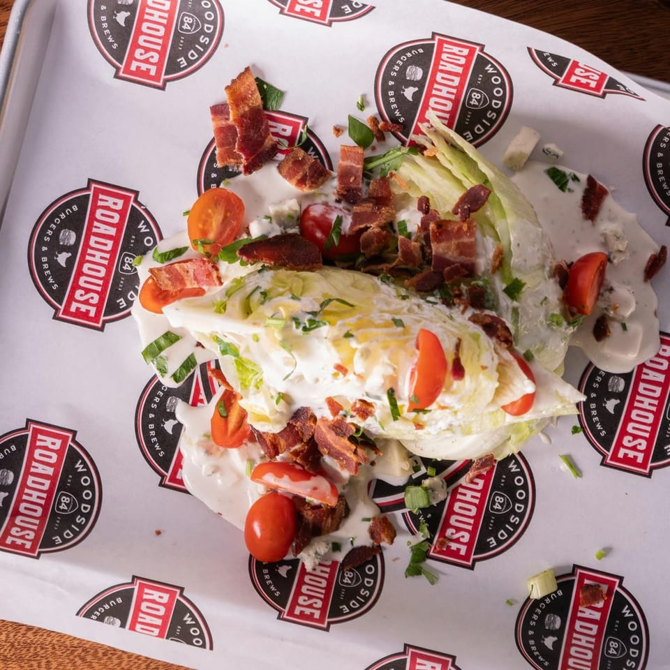 Woodside Roadhouse wedge salad with bacon, tomatoes, and blue cheese dressing on branded paper.