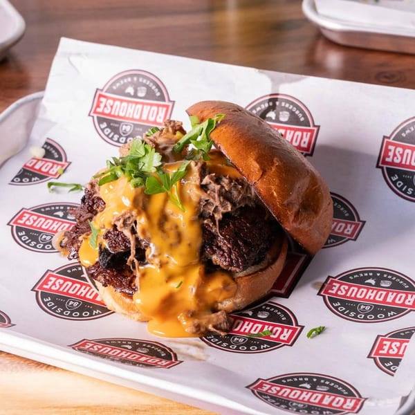 A Woodside Roadhouse pulled pork sandwich with cheese sauce and cilantro on branded paper.